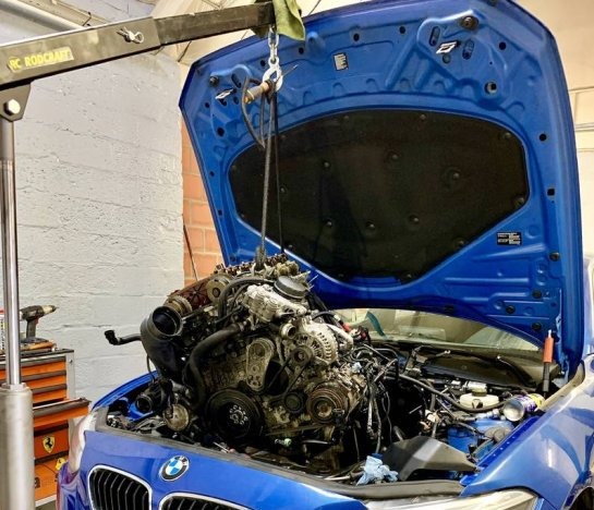 Een BMW in de werkplaats met geopende motorkap en de motor aan een kraan
